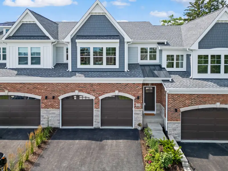 Exterior view of a luxury townhome with brick facade, stone accents, and attached three-car garage
